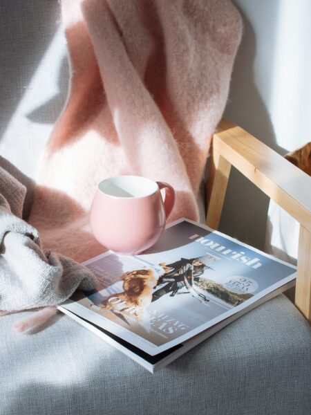 Cozy chair with soft blanket, mug, and magazine titled "nourish".